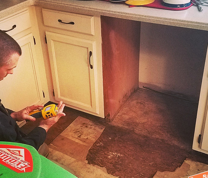 Technician with a yellow device to measure water, mold under a cabinet on the flooring