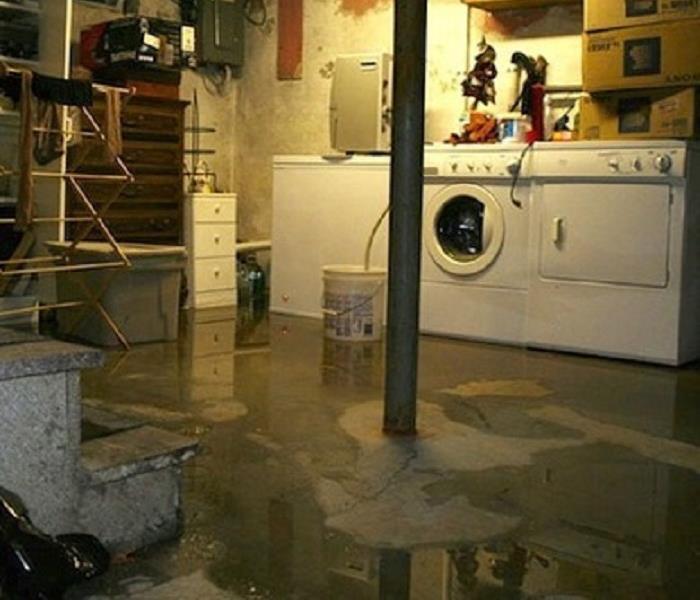 Water on a basement floor, in the background there is a washer and dryer